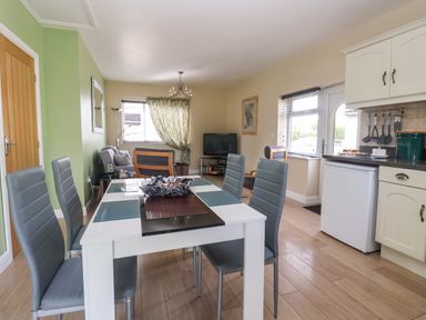 A dining area with a white table and gray chairs leading to a living room with a sofa and a TV at Church View in Atwick