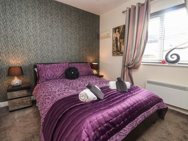 A bedroom with a bed covered in purple bedding two bedside tables with lamps a window with striped curtains and a wall painting at Church View in Atwick