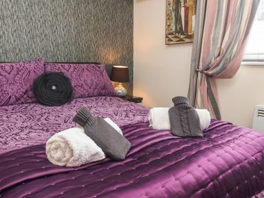 A bedroom with a purple bedspread pillows bedside table with lamp and towels with hot water bottles on the bed at Church View in Atwick
