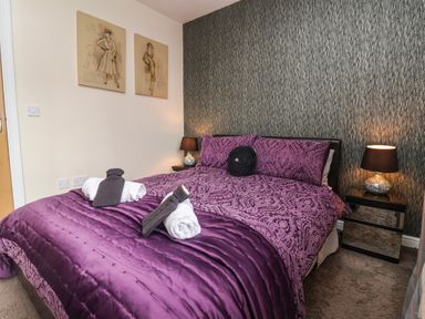 A bedroom with a double bed covered with purple bedding bedside tables with lamps and two framed sketches on wall at Church View in Atwick