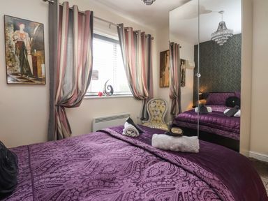 A bedroom with a purple bedspread a window with striped curtains a chair with floral upholstery and a mirrored wardrobe at Church View in Atwick