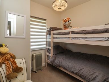 A small bedroom with bunk beds grey bedding a stuffed tiger on the top bunk a stuffed giraffe on a chair a heater and a window with blinds at Church View in Atwick