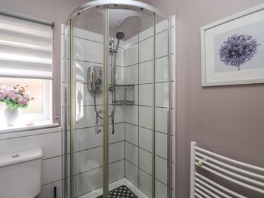 A bathroom with a glass shower enclosure a toilet a window with flowers on the sill a white towel radiator and framed artwork at Church View in Atwick