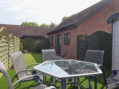 A backyard with a glass table and four metal chairs fenced by wooden panels at Church View in Atwick