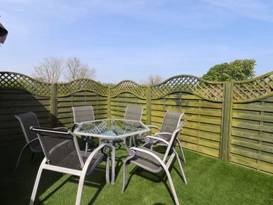 A patio area with six metal mesh chairs around a glass square table on artificial grass surrounded by wooden lattice fencing at Church View in Atwick