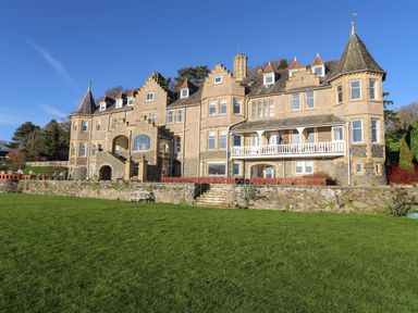 A large stone building with multiple windows and two towers overlooking a grassy lawn at Bryn Mel Manor Straits View in Menai Bridge