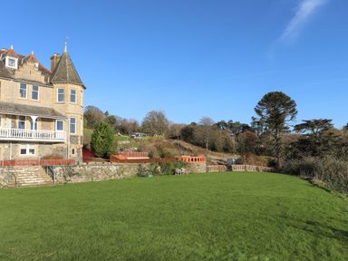 A stone house with a turret and a large grassy lawn surrounded by trees at Bryn Mel Manor Straits View in Menai Bridge