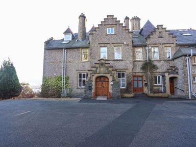 Stone building with multiple chimneys and wooden doors in front of a paved driveway at Bryn Mel Manor Straits View Menai Bridge