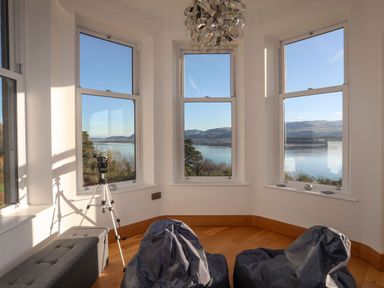 A room with three windows overlooking water and hills with a telescope on a tripod and two bean bags at Bryn Mel Manor Straits View Menai Bridge