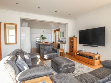 A living room with grey sofas a large TV on the wall a wooden TV stand and an open kitchen at Bryn Mel Manor Straits View Menai Bridge