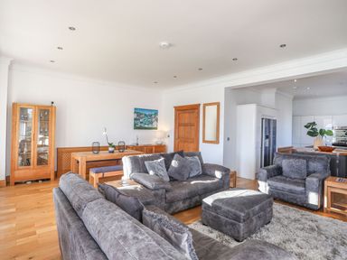 A living room with gray sofas and an ottoman near a wooden dining table and a glass cabinet at Bryn Mel Manor Straits View Menai Bridge