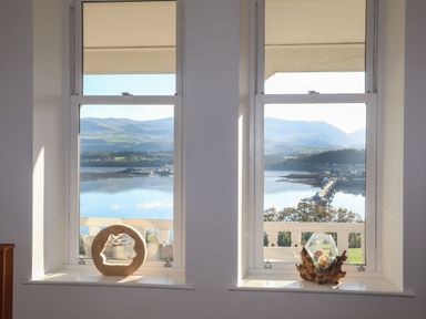 A pair of windows with decorative objects on the sills overlooking a lake and mountains at Bryn Mel Manor Straits View in Menai Bridge