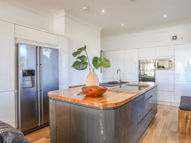 A kitchen with a large island with a wooden countertop a plant in a vase a wooden bowl a stainless steel refrigerator and built in oven and microwave at Bryn Mel Manor Straits View in Menai Bridge