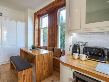 A kitchen with wooden table and bench seating by tall windows and black SMEG appliances at Bryn Mel Manor Straits View Menai Bridge