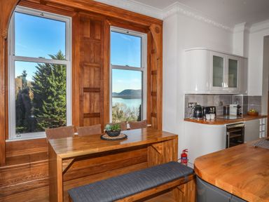 A kitchen with wooden dining table bench seating and white cabinets with windows showing a view at Bryn Mel Manor Straits View Menai Bridge