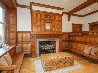 A room with wooden wall paneling a wooden bench with cushions a wooden coffee table and a fireplace with flowers at Bryn Mel Manor Straits View in Menai Bridge
