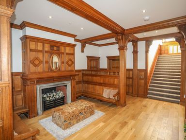 A wood paneled room with a fireplace a bench a wooden table on a rug and stairs at Bryn Mel Manor Straits View Menai Bridge