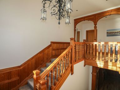 A wooden staircase with balustrades and a hanging chandelier at Bryn Mel Manor Straits View Menai Bridge
