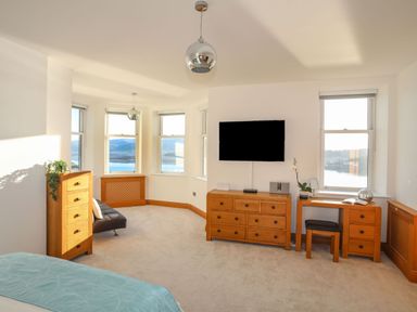 A bedroom with wooden furniture a wall mounted tv and windows overlooking water at Bryn Mel Manor Straits View Menai Bridge