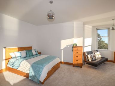 A bedroom with a wooden bed with blue and white bedding a wooden chest of drawers and a black sofa with pillows beside a window at Bryn Mel Manor Straits View Menai Bridge