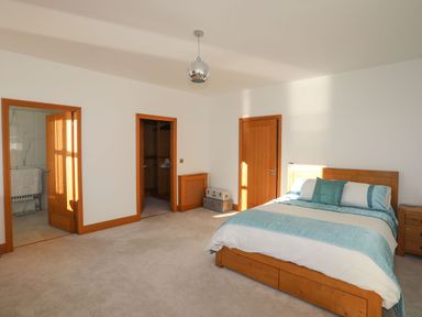 A bedroom with a wooden bed and blue bedding three wooden doors and carpeted floor at Bryn Mel Manor Straits View Menai Bridge