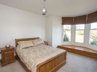 A bedroom with a wooden bed and two bedside tables next to a bay window with brown blinds at Bryn Mel Manor Straits View in Menai Bridge
