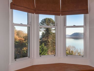 A bay window with brown blinds overlooking trees and a body of water at Bryn Mel Manor Straits View Menai Bridge