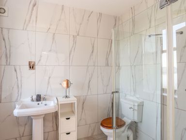 A bathroom with a pedestal sink a small storage unit a toilet with a wooden seat and a glass shower enclosure at Bryn Mel Manor Straits View in Menai Bridge