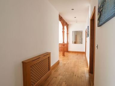 A hallway with wooden flooring wooden doors a wooden radiator cover and a mirror on the wall at Bryn Mel Manor Straits View Menai Bridge