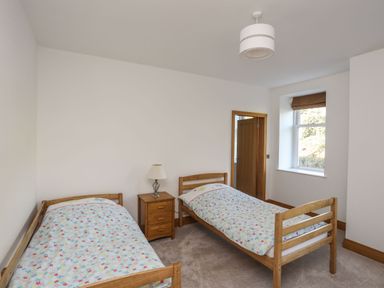 A bedroom with two single wooden beds a wooden nightstand with a lamp and a window at Bryn Mel Manor Straits View in Menai Bridge