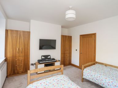 A bedroom with two beds and floral bedspreads with a keyboard on a stand and a wall mounted tv at Bryn Mel Manor Straits View Menai Bridge