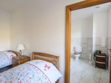 A bedroom with two single beds and a nightstand next to an open doorway leading to a bathroom with a toilet and a wicker storage unit at Bryn Mel Manor Straits View Menai Bridge