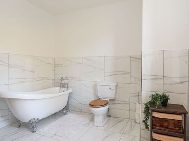 A bathroom with a freestanding clawfoot bathtub a toilet with a wooden seat and a wooden storage unit with plants at Bryn Mel Manor Straits View Menai Bridge