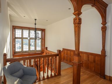 A staircase with wooden railings a carved wooden arch a gray armchair and a window with decorative glass at Bryn Mel Manor Straits View Menai Bridge