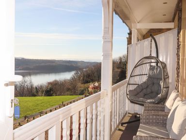 A balcony with a hanging chair a wicker sofa and a view of a river and trees at Bryn Mel Manor Straits View Menai Bridge
