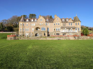 A large stone manor house with turrets and multiple windows facing a wide lawn at Bryn Mel Manor Straits View in Menai Bridge