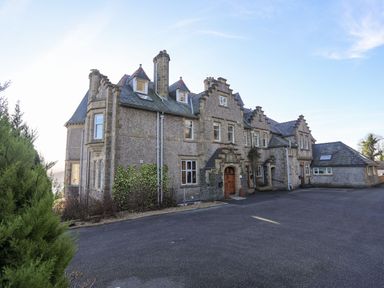 A large stone building with multiple chimneys and gabled windows with a paved area in front at Bryn Mel Manor Straits View Menai Bridge