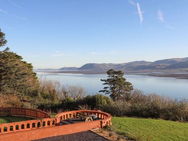 A garden with a curved red brick wall and bench overlooking a body of water with hills in the background at Bryn Mel Manor Straits View Menai Bridge
