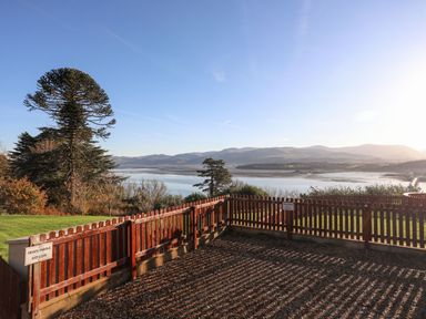 A fenced gravel area overlooking a body of water with hills in the background at Bryn Mel Manor Straits View in Menai Bridge