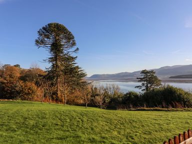 A grassy lawn with trees and a body of water with hills in the distance at Bryn Mel Manor Straits View Menai Bridge