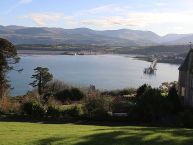 A waterfront view with a pier extending into the water and hills in the background at Bryn Mel Manor Straits View Menai Bridge