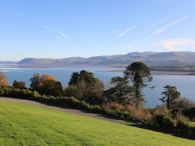 A view of a body of water with trees in the foreground and hills in the background at Bryn Mel Manor Straits View Menai Bridge