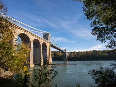 A suspension bridge over a river with trees on both sides at Bryn Mel Manor Straits View Menai Bridge