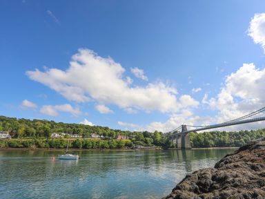 A sailboat on water near a bridge with houses and trees in the background at Bryn Mel Manor Straits View in Menai Bridge