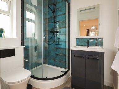 A bathroom with a corner shower with blue tiles a toilet and a sink with a mirror at Pheasant View in Penelewey near Carnon Downs