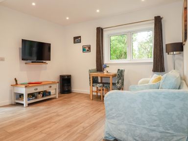 A living room with a sofa table and chairs a wall-mounted TV and a window at Pheasant View in Penelewey near Carnon Downs