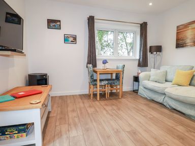 A living room with a light blue sofa a wooden table with two chairs a wall-mounted television and wooden flooring at Pheasant View in Penelewey near Carnon Downs