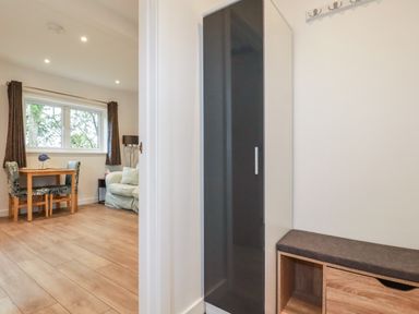 A room with a black and white wardrobe and a wooden bench with a cushion next to a living area with a small wooden table and two chairs at Pheasant View in Penelewey near Carnon Downs