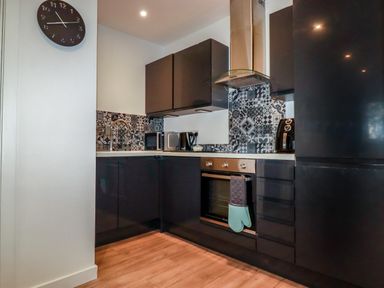 A kitchen with black cabinets a patterned tile backsplash a clock and kitchen appliances at Pheasant View in Penelewey near Carnon Downs