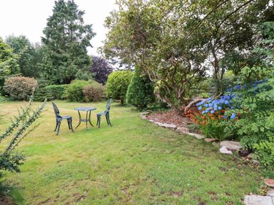 A garden with a metal table and two chairs surrounded by bushes flowers and trees at Pheasant View in Penelewey near Carnon Downs